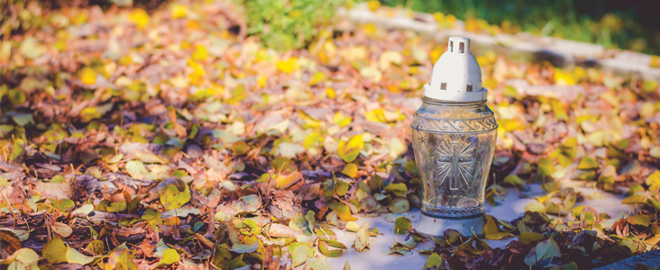 Glass lantern with cross on it surrounded by brown and yellow leaves