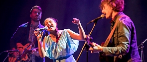 A female performer belts out a song on stage while accompanied by her band