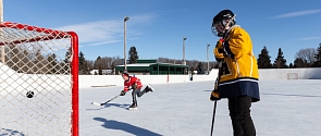 Two kids play hockey at an outdoor rink on beautiful day