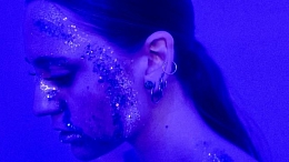 Stephanie Hayden posed in front of a blue background with glitter makeup