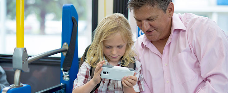Picture of a man and girl sitting on a bus looking at the screen of a phone