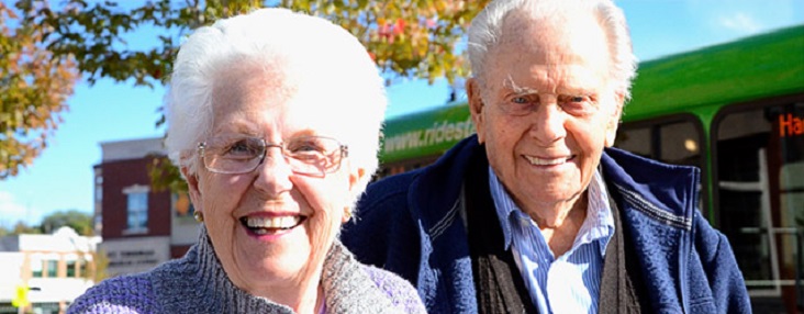 Photo of an elderly couple standing in front of a Handibus smiling