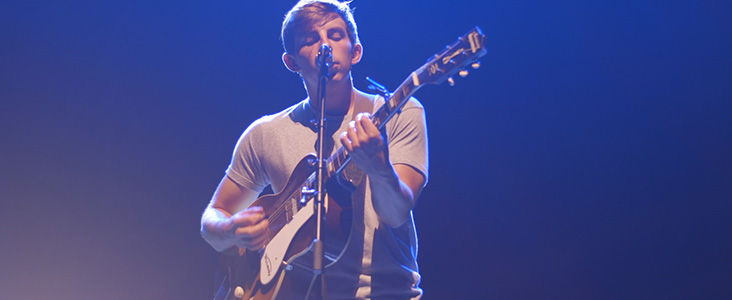 Photo of performer singing and playing guitar