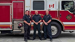 Image of three firefighters standing in front of a red and white fire truck with a ladder on top.