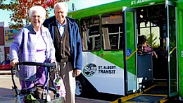 A senior couple stand in front of a Handibus